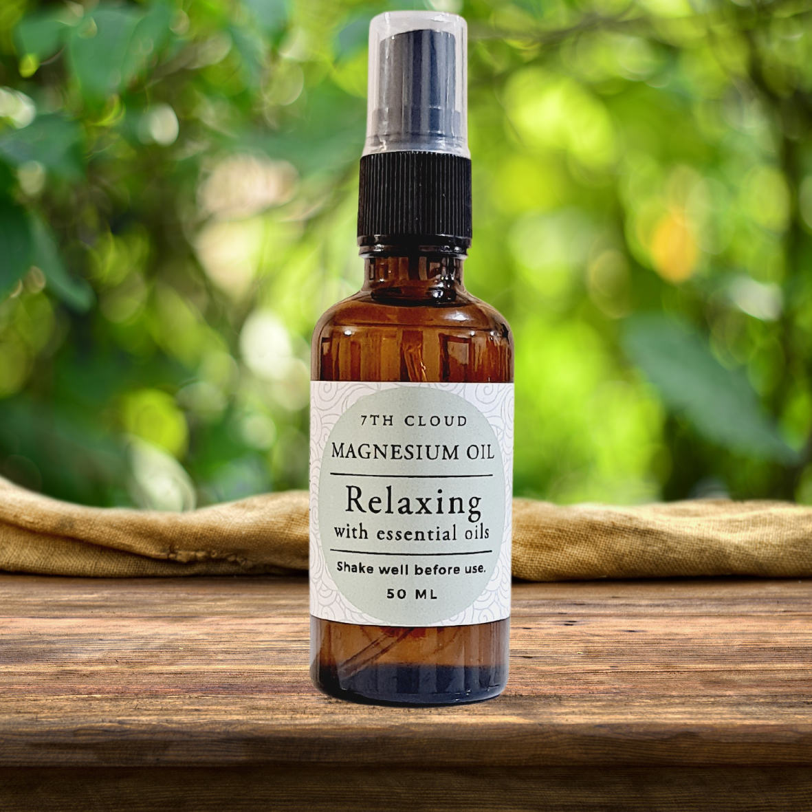 A 50ml amber glass bottle of magnesium oil relaxing spray with essential oils, labeled '7th Cloud Magnesium Oil Relaxing' and placed on a wooden surface in a natural outdoor setting.