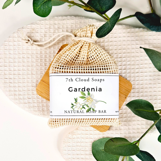 7th Cloud Soaps Gardenia natural soap bar in a mesh bag with green leaves on a light background
