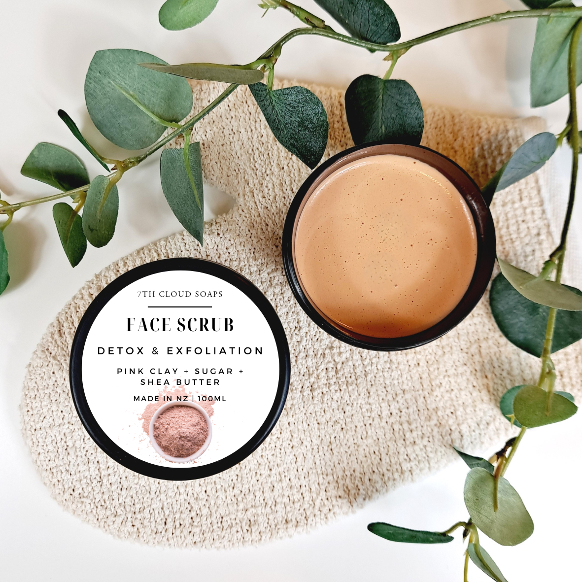7th Cloud Soaps face scrub with a container and packaging on a textured surface with green leaves.