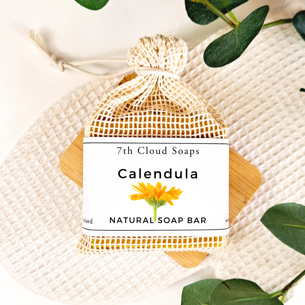 7th Cloud Soaps Calendula Natural Soap Bar in a mesh bag with green leaves on a light background