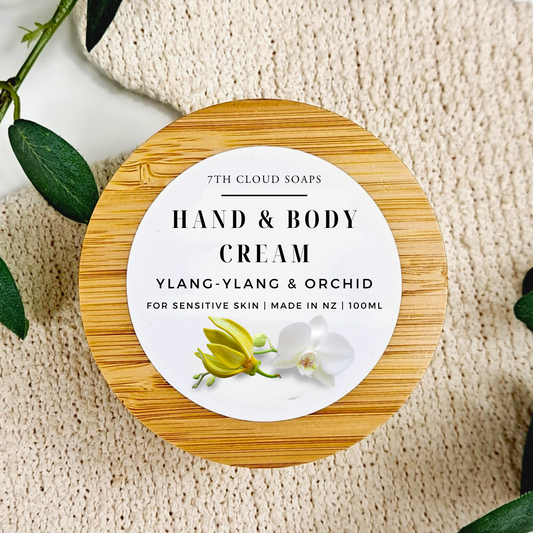 Hand and body cream container with bamboo lid on a textured surface with green leaves.