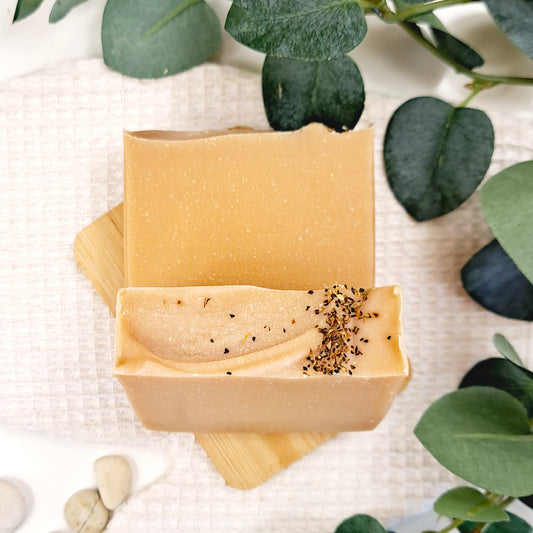 Bar of soap in a brown wooden soap dish with green leaves in the background