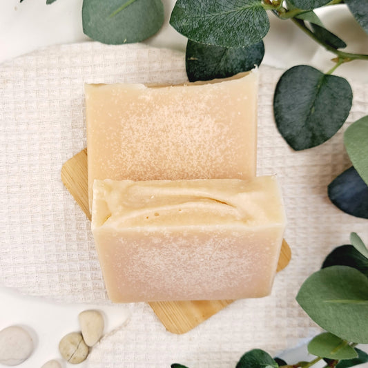 Two bars of soap on a wooden block with green leaves in the background