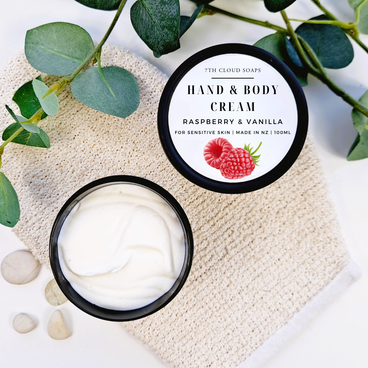 Hand and body cream with raspberry and vanilla flavor on a textured surface with green leaves.