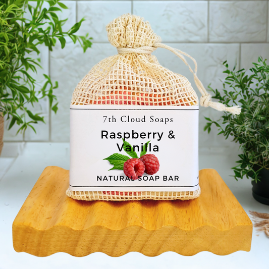 7th Cloud Soaps Raspberry & Vanilla natural soap bar in a mesh bag on a wooden block with plants in the background.