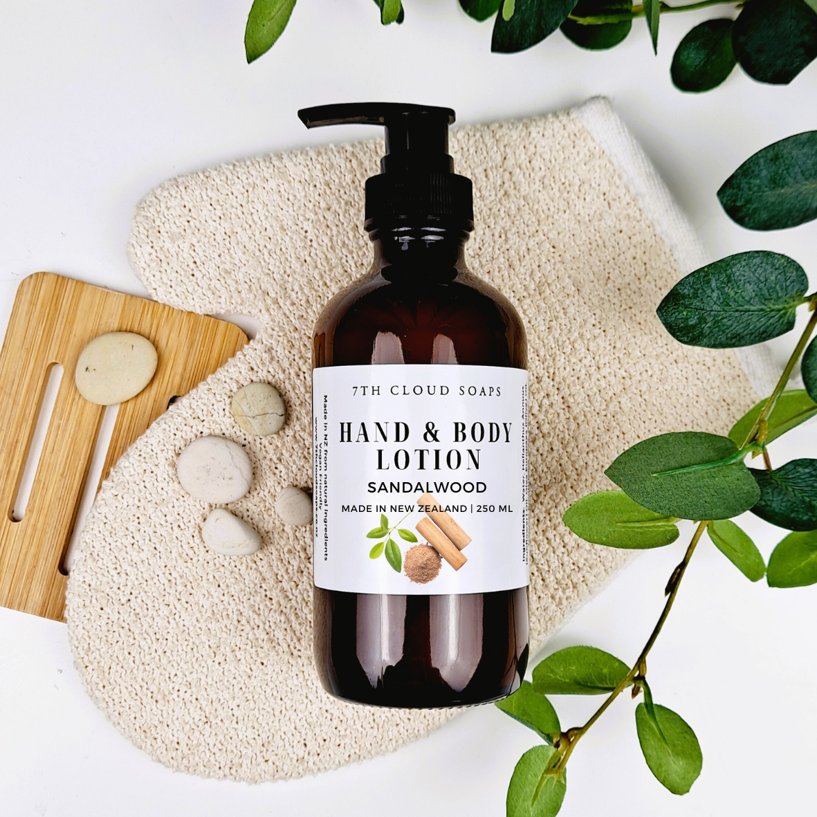 A bottle of hand and body lotion with a pump, labeled '5th Cloud Soaps Sandalwood Lotion', placed on a wooden surface with a pumice stone and leaves in the background.