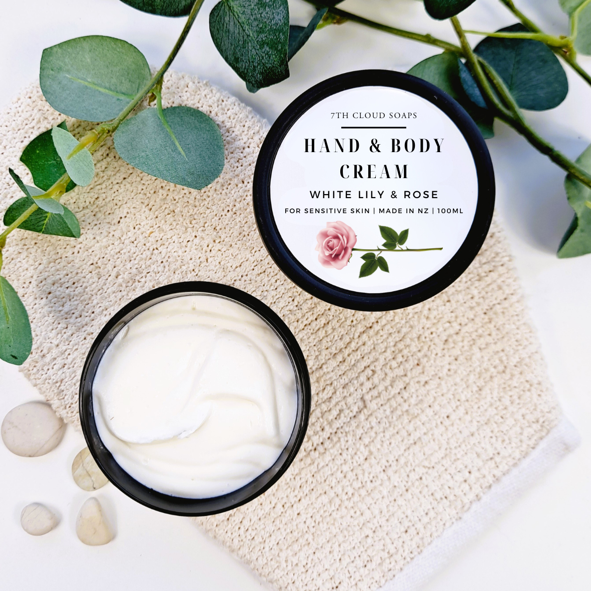 Hand and body cream with a floral label on a textured surface with green leaves.