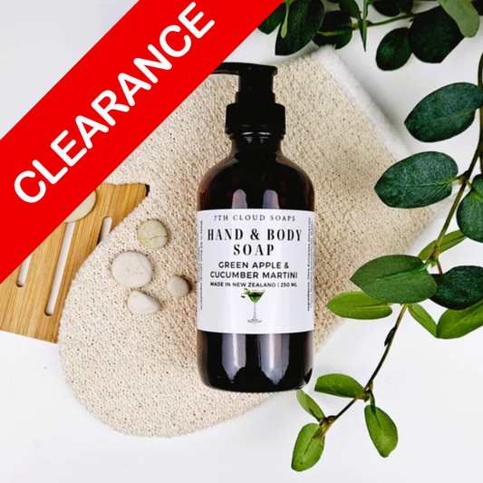 Hand and body soap bottle with a label on a textured surface with green leaves and a 'Clearance' sign.