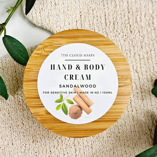 Hand and body cream container with sandalwood fragrance on a textured surface.