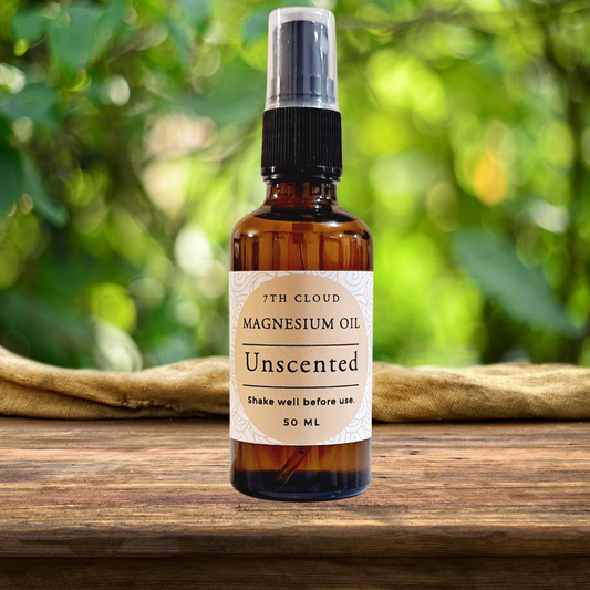 A 50ml amber glass bottle of magnesium oil with a mist spray cap, labeled 'Magnesium Oil Unscented', placed on a wooden surface with greenery in the background.