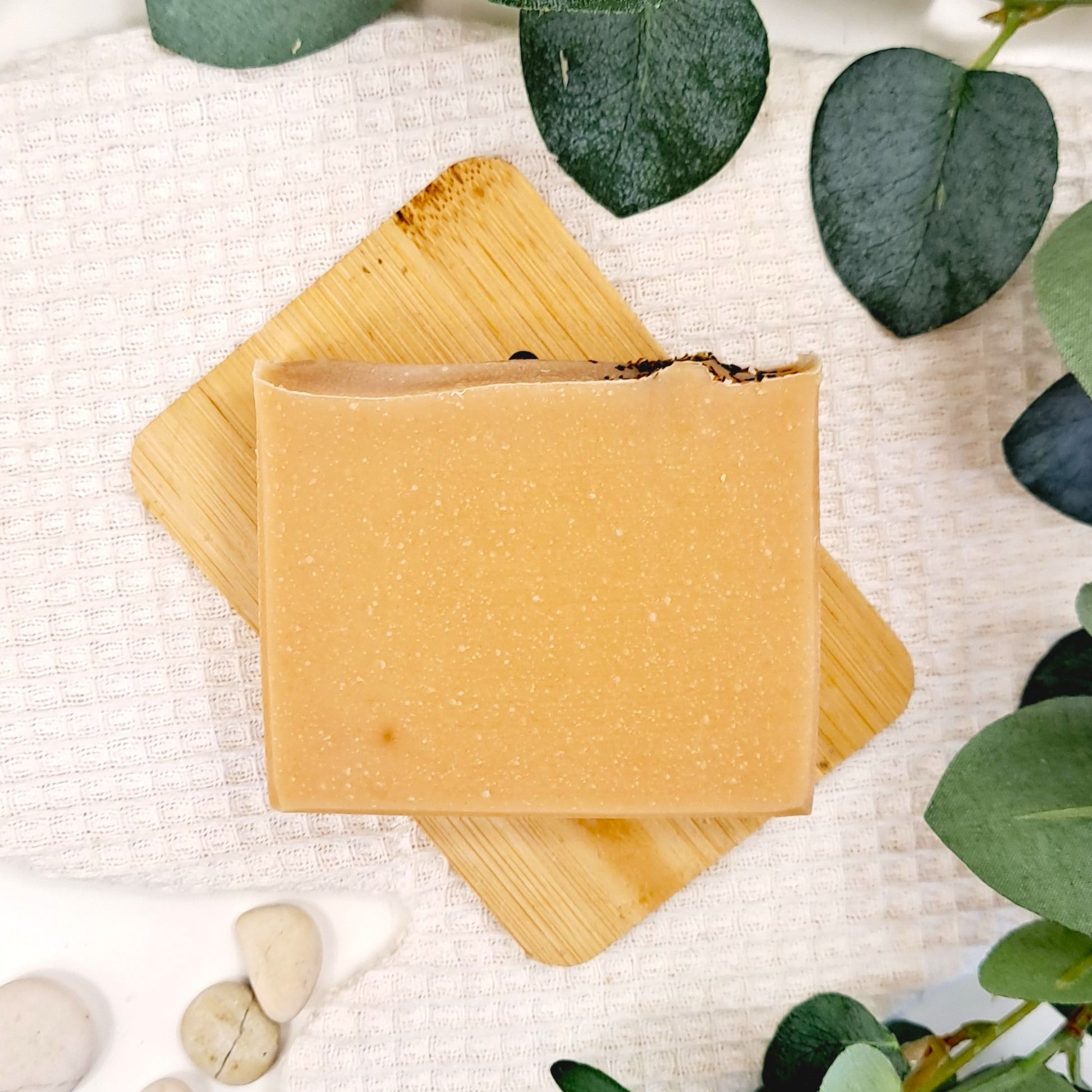 Two bars of natural soap on a wooden board with green leaves and stones in the background