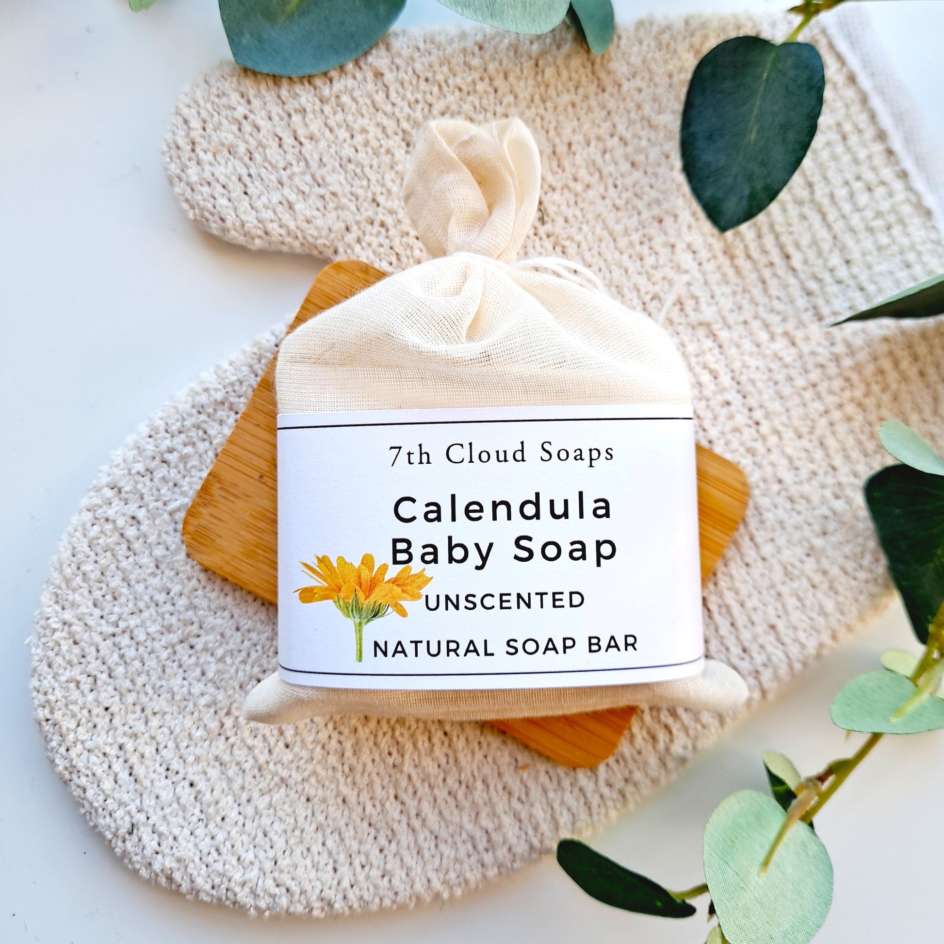 7th Cloud Soaps Calendula Baby Soap on a textured surface with green leaves.