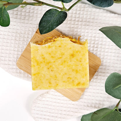 Yellow soap on a wooden block with green leaves around on a white textured background