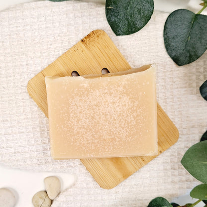 Bar of soap on a wooden soap dish with green leaves in the background