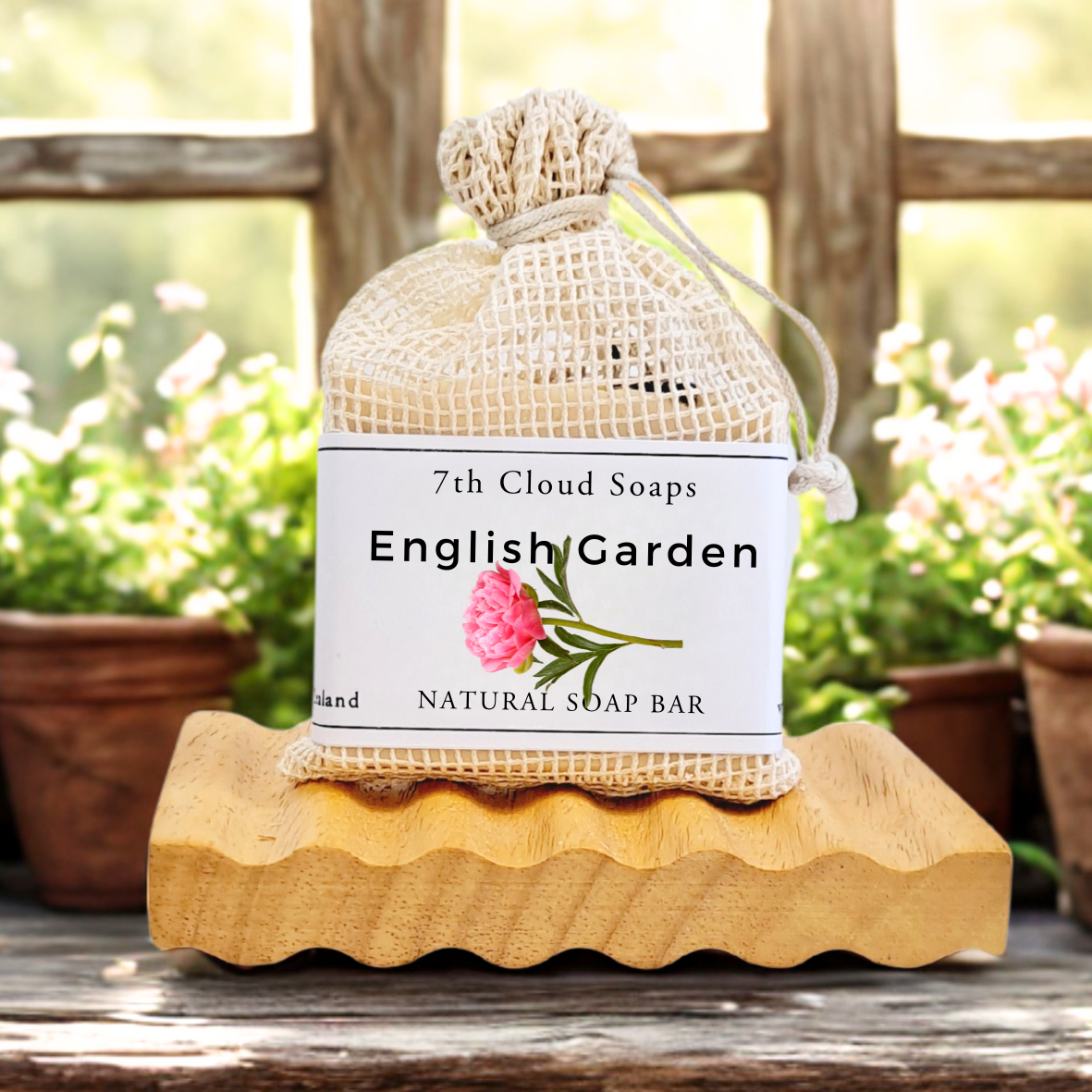 7th Cloud Soaps English Garden natural soap bar in a mesh bag on a wooden stand with plants in the background