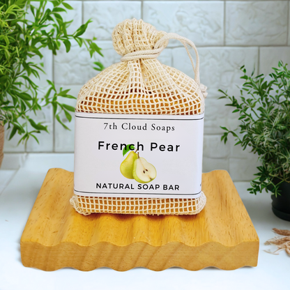 A natural soap bar labeled 'French Pear' from 7th Cloud Soaps, packaged in a beige mesh net, placed on a wooden surface with a plant in the background.