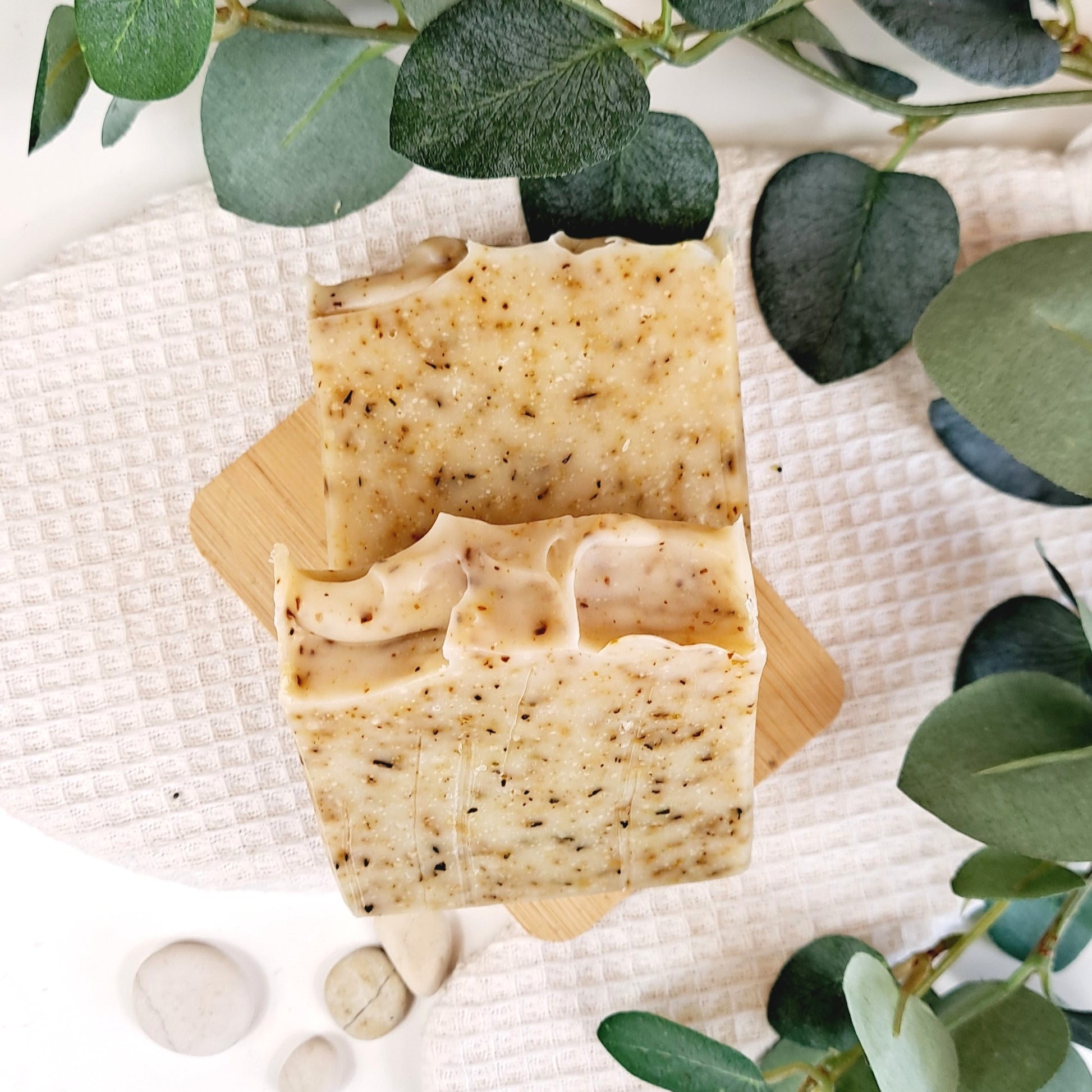 Two soap bars on a wooden stand with green leaves in the background