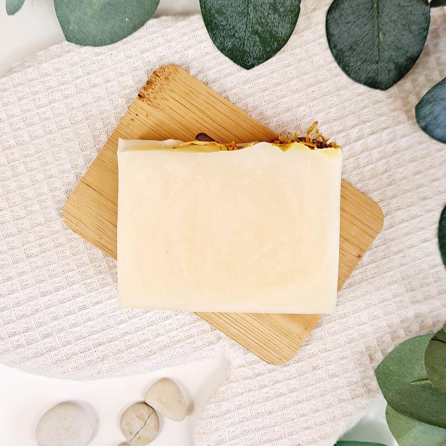 Bar of soap on a wooden block with green leaves and stones in the background