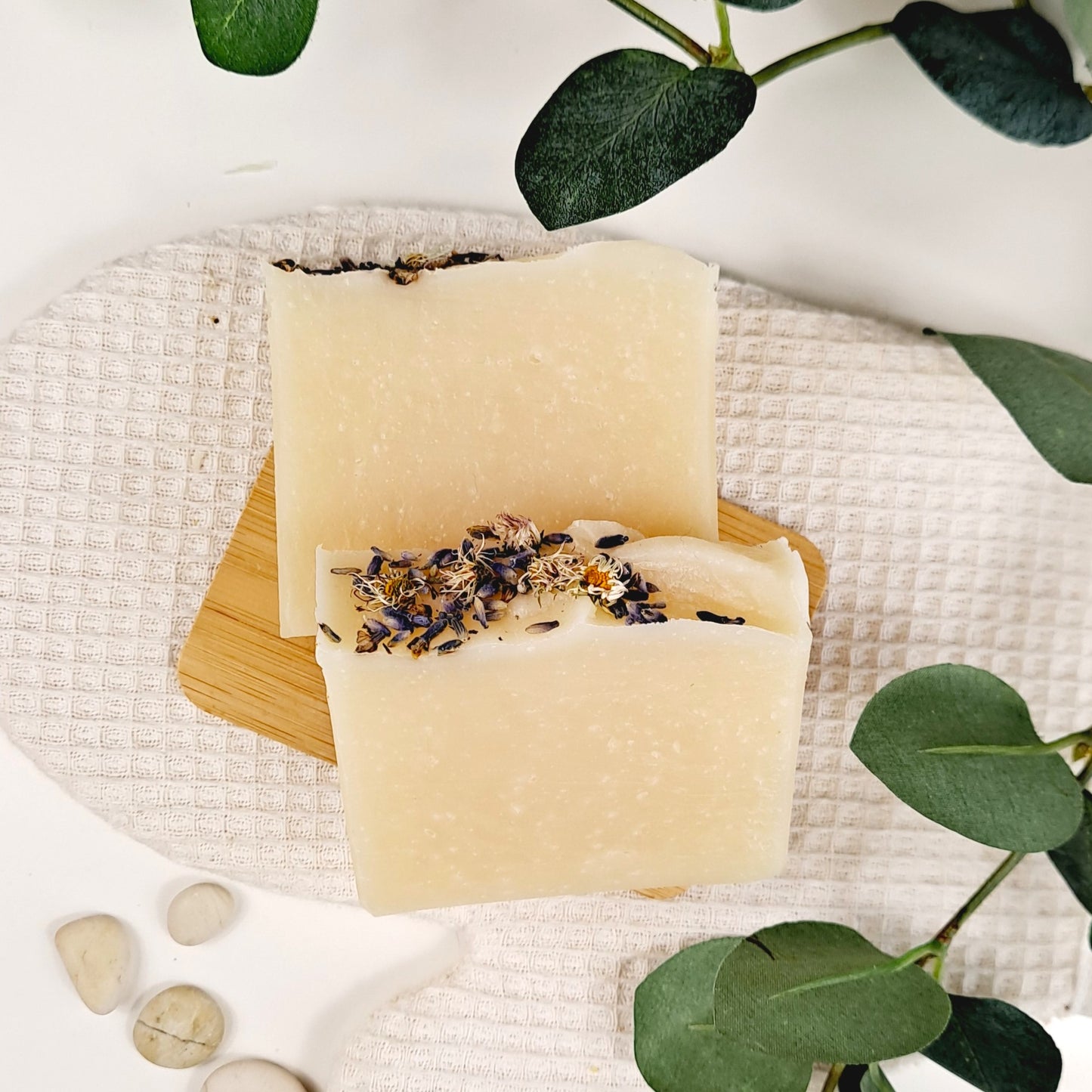 Two bars of soap with visible ingredients on a woven mat with green leaves in the background