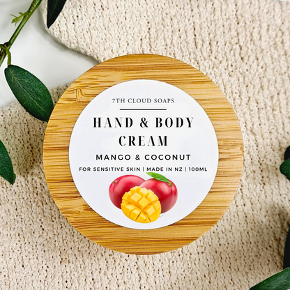 Hand and body cream container with a wooden lid on a textured surface, featuring mango and coconut illustration.