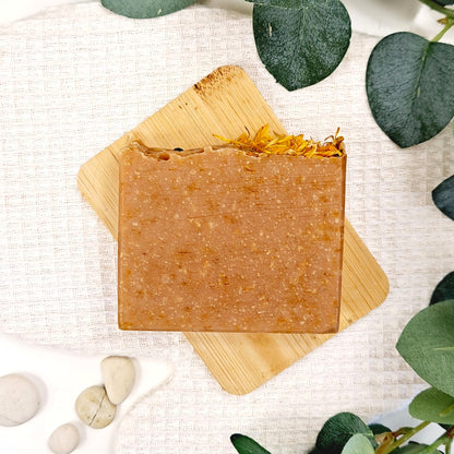 Bar of soap on a wooden board with green leaves and stones in the background
