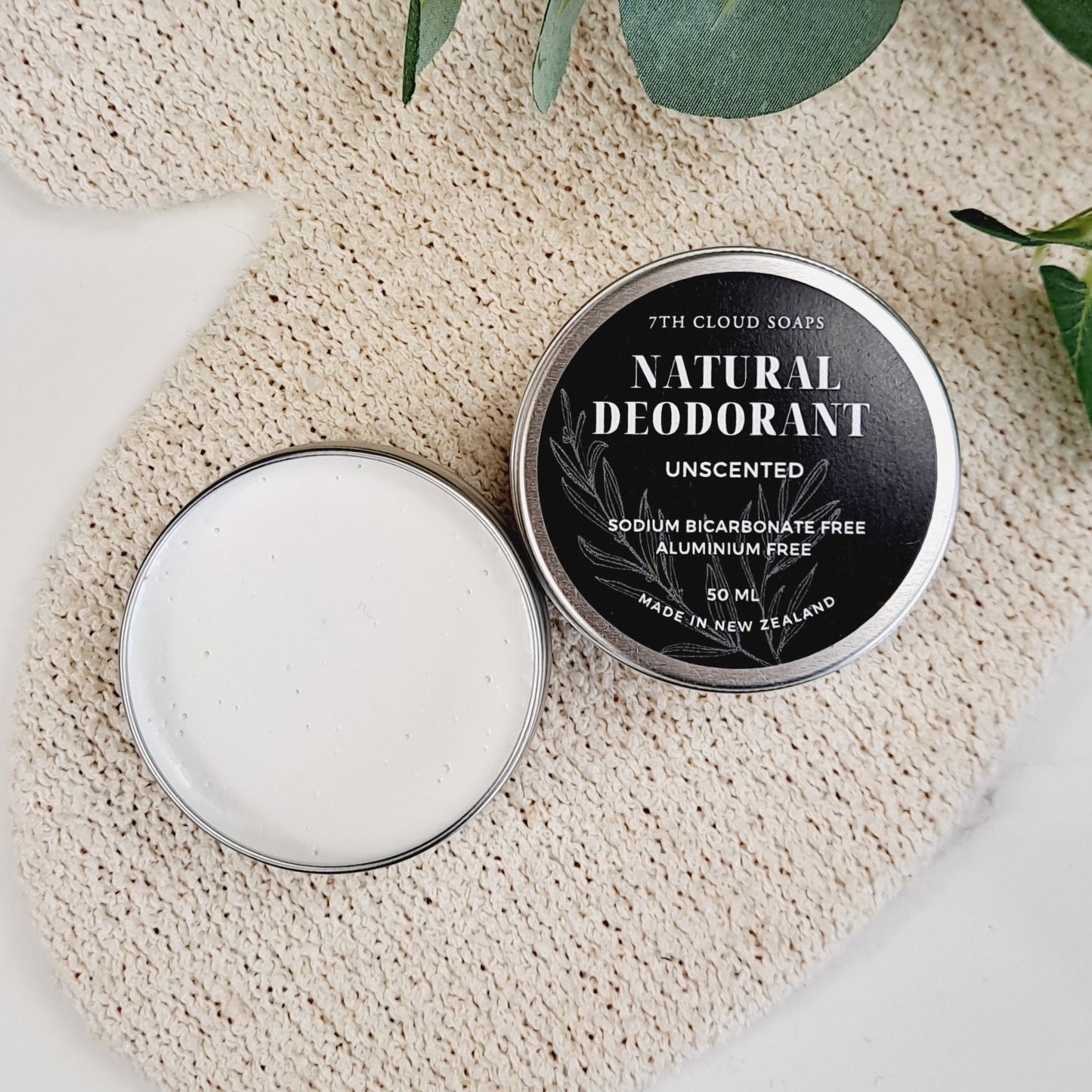 A container of natural deodorant cream open to show the product, with the label on the lid indicating it is unscented, sodium bicarbonate free, and aluminum free.