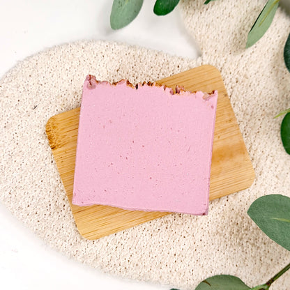 Pink soap bar on a wooden board with green leaves in the background