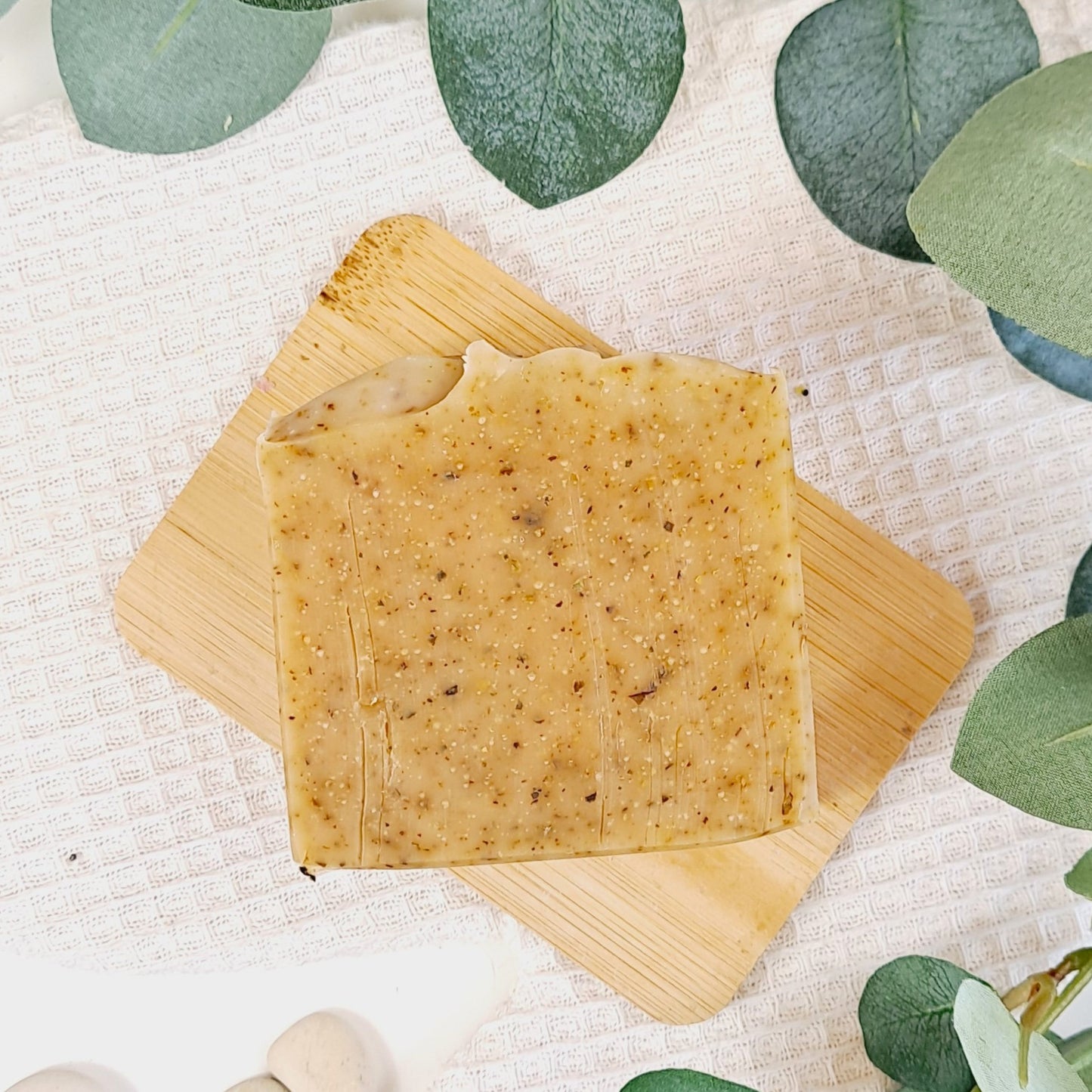 Bar of soap on a wooden soap dish with green leaves in the background