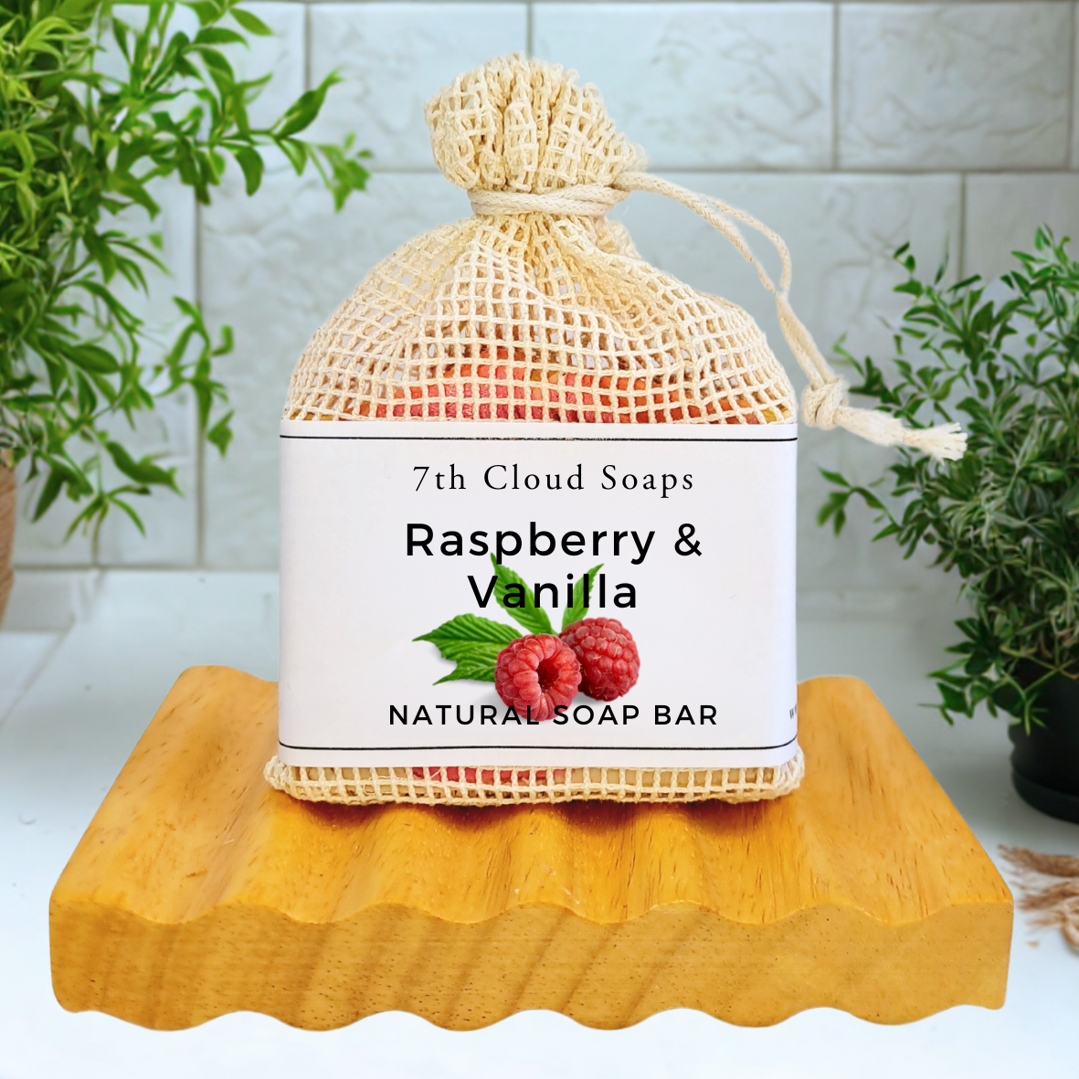7th Cloud Soaps Raspberry & Vanilla natural soap bar in a mesh bag on a wooden block with plants in the background.