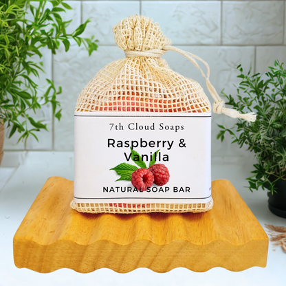 7th Cloud Soaps Raspberry & Vanilla natural soap bar in a mesh bag on a wooden block with plants in the background.