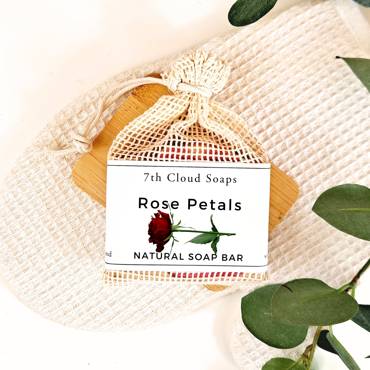 7th Cloud Soaps Rose Petals Natural Soap Bar in a drawstring bag on a textured fabric background with green leaves.