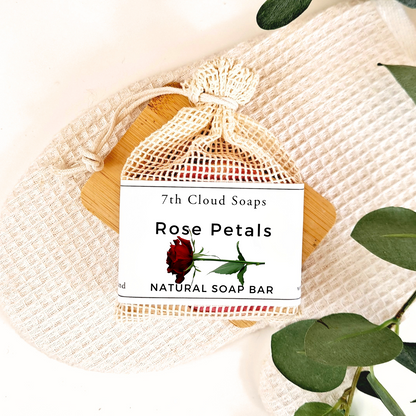 7th Cloud Soaps Rose Petals Natural Soap Bar in a drawstring bag on a textured fabric background with green leaves.