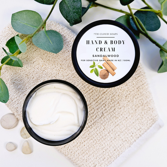 Hand and body cream in a jar with a label on a textured surface with green leaves.