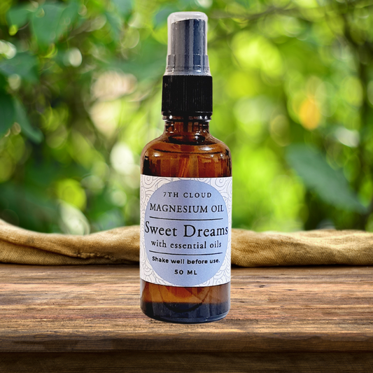 A 50ml amber glass bottle of magnesium oil with a mist spray cap, labeled 'Sweet Dreams' accompanied by essential oils. The bottle is placed on a wooden surface with greenery in the background.