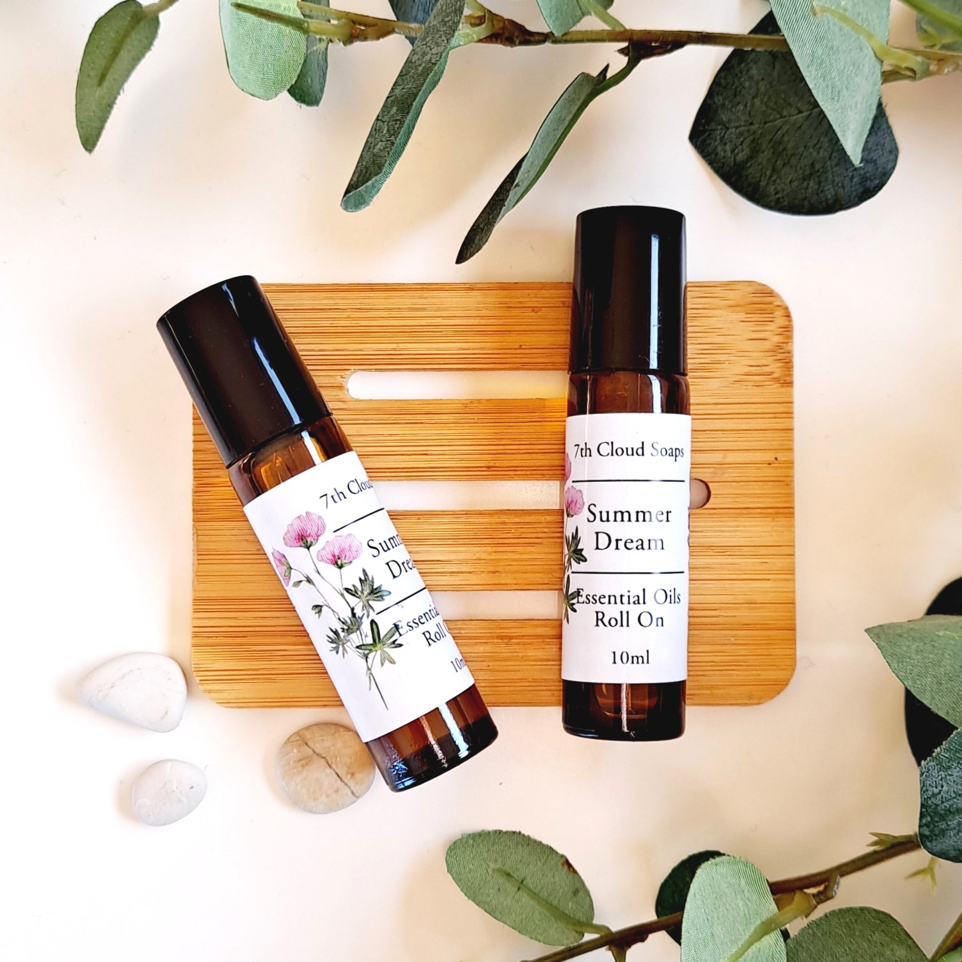 Two aromatherapy roll-on bottles labeled 'Summer Dream' and '7th Cloud Soap', containing essential oils for anxiety and stress relief, with one standing upright and the other lying down on a wooden board, surrounded by decorative leaves and petals.