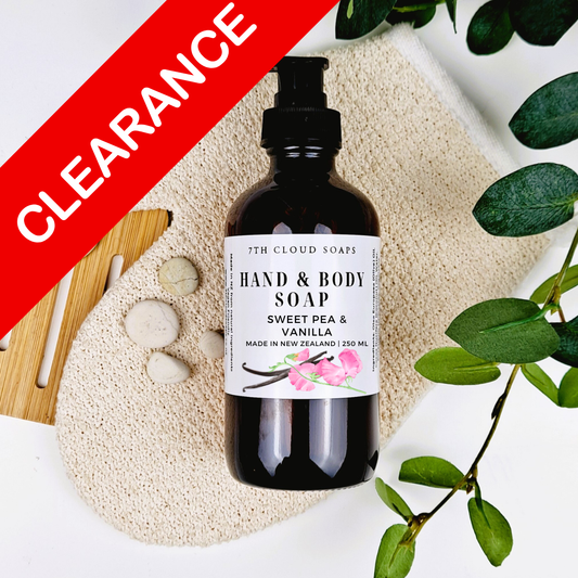 Hand and body soap bottle with a label on a textured surface with green leaves.