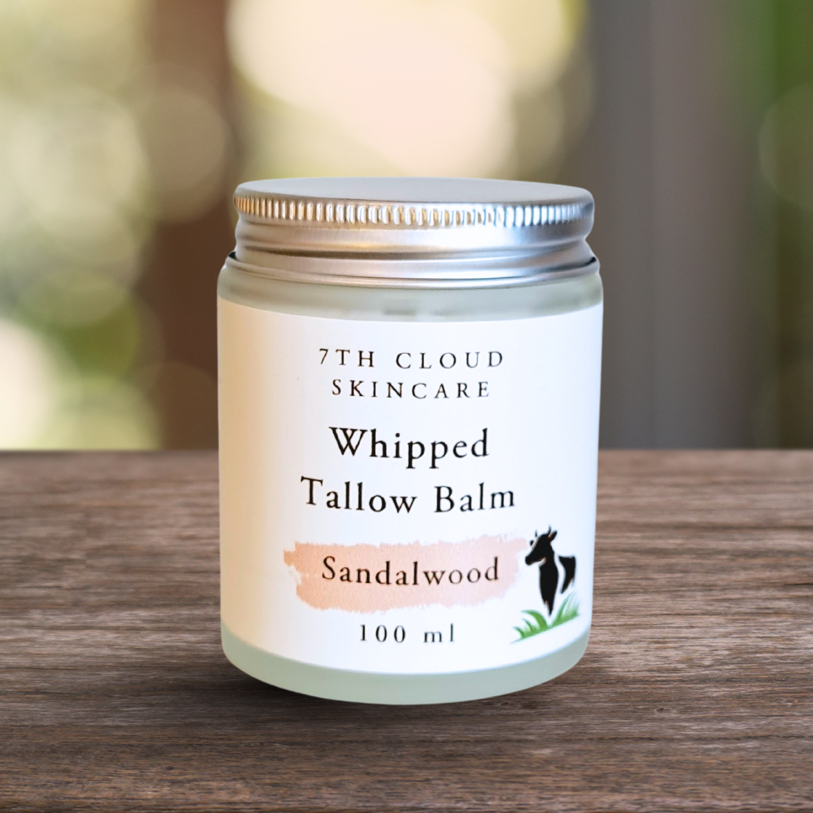 Jar of 7th Cloud Skincare Whipped Tallow Balm Sandalwood on a wooden surface with a blurred natural background